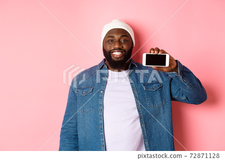 Online shopping and technology concept. Handsome Black man showing smartphone screen horizontally and smiling satisfied, recommending app, pink background 72871128