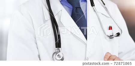 Unknown male doctor iusing tablet computer in his hands, while standing in sunny clinic. Medicine concept during Coronavirus pandemic. Covid-2019 72871865
