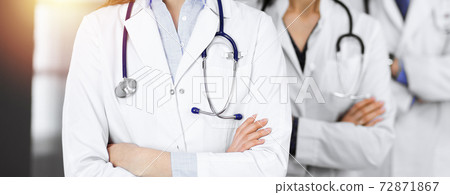 Group of professional doctors is standing as a team with arms crossed in sunny clinic. Medicine concept during Coronavirus pandemic. Covid-2019 Group of professional doctors is standing as a team with arms crossed in sunny clinic. Medicine concept during Coronavirus pandemic. Covid-2019 72871867