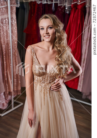 Beautiful blonde girl wearing a full-length yellow champaign chiffon slit prom ball gown decorated with golden sequins. Model in dress hire service with many dresses in different color and style. Beautiful blonde girl wearing a full-length yellow champaign chiffon slit prom ball gown decorated with golden sequins. Model in dress hire service with many dresses in different color and style. 72872467