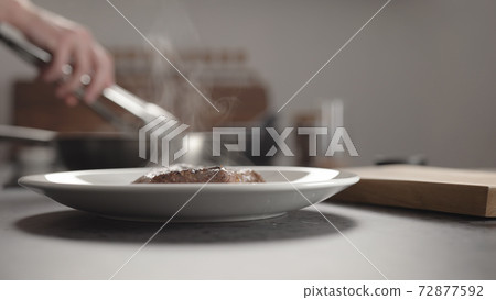 Man hand put cooked steak on white plate for resting before serving 72877592