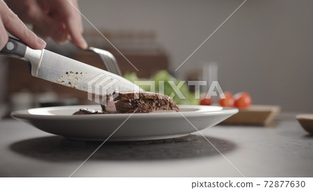 Closeup man slicing steak on white plate on kitchen countertop 72877630