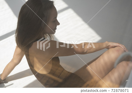 Portrait of happy young skinny brunette woman posing in black underwear, sitting on a white floor in white studio with shadows from a window. Model tests of pretty girl in basic clothes on cyclorama. Portrait of happy young skinny brunette woman posing in black underwear, sitting on a white floor in white studio with shadows from a window. Model tests of pretty girl in basic clothes on cyclorama. 72878071