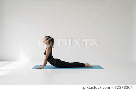 Young woman practicing yoga, lying and stretching in Cobra pose, doing Bhujangasana exercise. Attractive girl in black sportswear. Beautiful sporty fit yogini woman practices yoga asana bhujangasana. Young woman practicing yoga, lying and stretching in Cobra pose, doing Bhujangasana exercise. Attractive girl in black sportswear. Beautiful sporty fit yogini woman practices yoga asana bhujangasana. 72878804