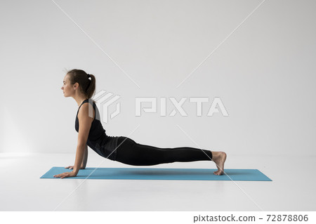Young woman practicing yoga, lying and stretching in Cobra pose, doing Bhujangasana exercise. Attractive girl in black sportswear. Beautiful sporty fit yogini woman practices yoga asana bhujangasana. Young woman practicing yoga, lying and stretching in Cobra pose, doing Bhujangasana exercise. Attractive girl in black sportswear. Beautiful sporty fit yogini woman practices yoga asana bhujangasana. 72878806