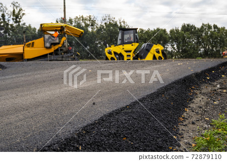Asphalt road roller with heavy vibration roller compactor press new hot asphalt on the roadway on a road construction site. Heavy Vibration roller at asphalt pavement working. Repairing. 72879110