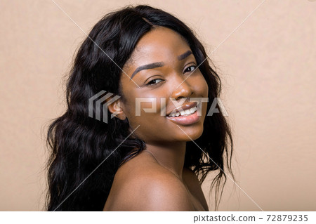 Portrait of smiling pretty young african american woman with natural makeup and long dark hair, looking at camera isolated on beige background. Beauty, skin care, people, races concept Portrait of smiling pretty young african american woman with natural makeup and long dark hair, looking at camera isolated on beige background. Beauty, skin care, people, races concept 72879235