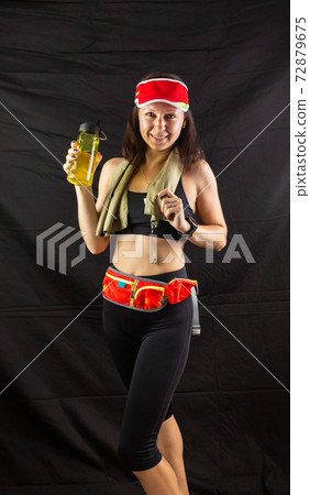 Beautiful girl in jogging red uniform, drinks water after training in the studio on a black background 72879675
