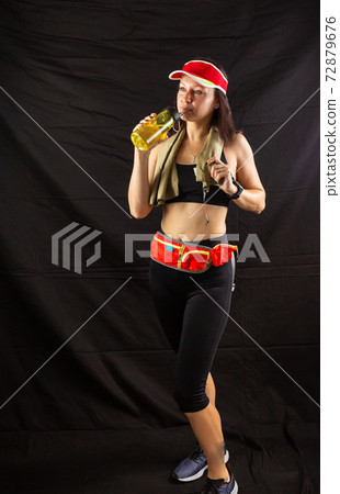Beautiful girl in jogging red uniform, drinks water after training in the studio on a black background Beautiful girl in jogging red uniform, drinks water after training in the studio on a black background 72879676