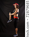 Beautiful girl in a jogging red uniform warming up before training in the studio on a black background 72879685