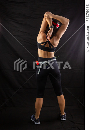 Beautiful girl in a jogging red uniform warming up before training in the studio on a black background 72879688