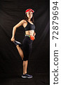 Beautiful girl in a jogging red uniform warming up before training in the studio on a black background 72879694