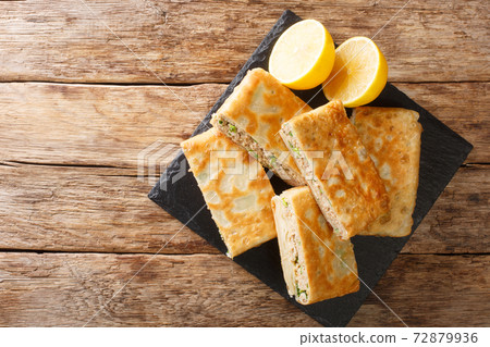 Tasty Mutabbaq Middle Eastern folded pan-fried flatbreads, stuffed with lightly spiced mince meat and egg closeup in the board. horizontal top view 72879936