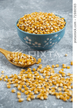 Uncooked corn kernels in blue bowl on marble surface 72880383