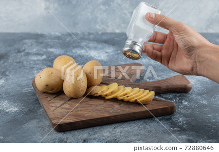 Man pouring salt over the sliced potatoes 72880646