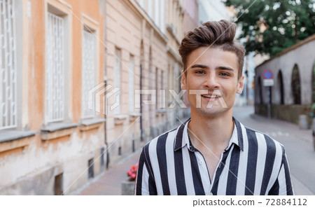 Young hipster man outdoors. Image of happy young man walking on the street and looking aside while. The guy on the street and looking at camera. Poland. Young hipster man outdoors. Image of happy young man walking on the street and looking aside while. The guy on the street and looking at camera. Poland. 72884112