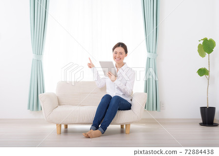 A woman pointing at a tablet on the sofa in the living room 72884438