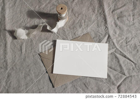 Wedding moody still life, table composition. Blank greeting card, invitation mockup scene with craft envelope and silk ribbon. Linen tablecloth background. Natural rustic design. 72884543