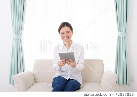A smiling woman looking at a tablet on the sofa in the living room trimming up A smiling woman looking at a tablet on the sofa in the living room trimming up 72885838