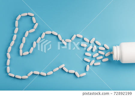 Vitamins from a white jar in the form of a biceps muscle on a blue background. Vitamins from a white jar in the form of a biceps muscle on a blue background. 72892199