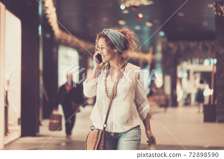 Cheerful trendy adul caucasian woman do a phone call while walk inside a commercial mall center looking for clothes and wear to buy - shopping leisure activity for people and business economy fashion Cheerful trendy adul caucasian woman do a phone call while walk inside a commercial mall center looking for clothes and wear to buy - shopping leisure activity for people and business economy fashion 72898590