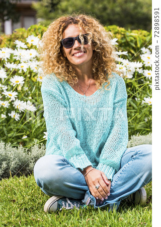 Happy and cheerful beautiful caucasian adult woman enjoy the park and smile at the camera with green natural daisy in background - spring and flower season and people happy portrait concept 72898591