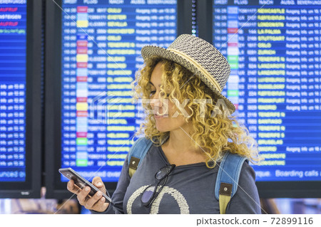 Portrai of beautiful adult caucasian woman travel and check app on smart phone to leave and start at the airport - displays with time in background - technology and internet connection modern 72899116