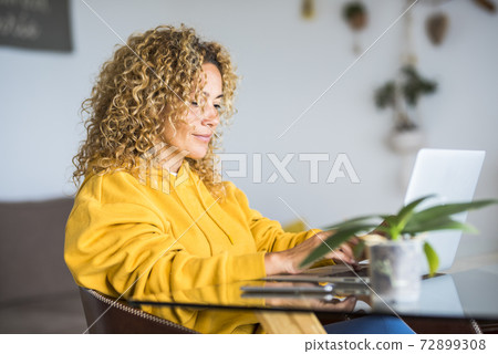 Adult pretty woman at home work with laptop computer on the table- concept of modern smart woking and job alternative office - blonde curly hair and beutiful people in technology internet connected 72899308