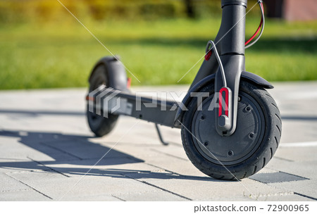 Electric scooter parked on tiled stone pavement - closeup detail on front wheel 72900965