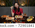 Woman is holding chopsticks with sushi opposite her eye 72901841