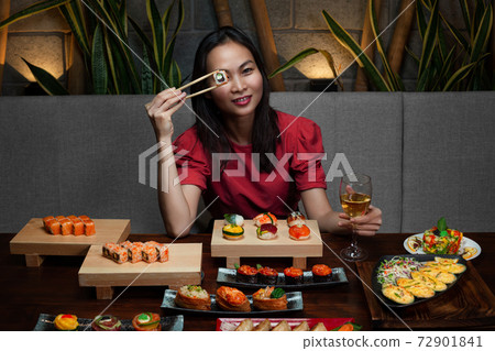 Woman is holding chopsticks with sushi opposite her eye Woman is holding chopsticks with sushi opposite her eye 72901841