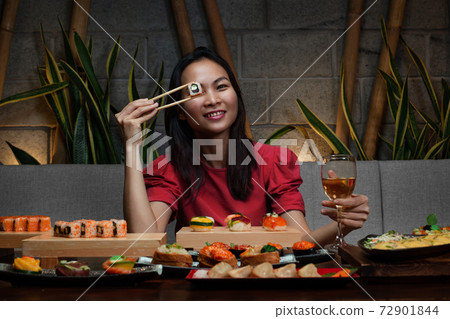 Woman is holding chopsticks with sushi opposite her eye Woman is holding chopsticks with sushi opposite her eye 72901844