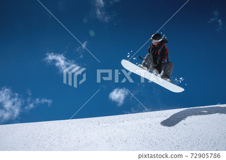 Woman athlete snowboarder in flight after jumping on a snowy slope against a background of a dark blue sky Woman athlete snowboarder in flight after jumping on a snowy slope against a background of a dark blue sky 72905786