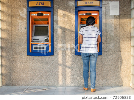A woman using automated teller machine. Young woman is withdrawing money from ATM on the street. 72906828