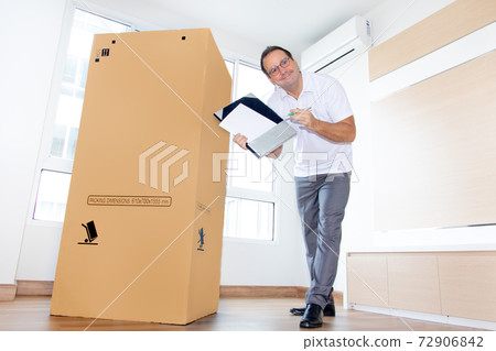 A man in an empty room shows a blank paper document for shipping large package. A man in an empty room shows a blank paper document for shipping large package. 72906842