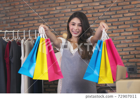 Young asian woman smile with success SME business  and shopping bag in hand for online shopping at home.. 72907011