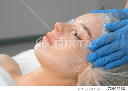 Cosmetologist doctor applies film on cream with anesthesia on woman's face. 72907588