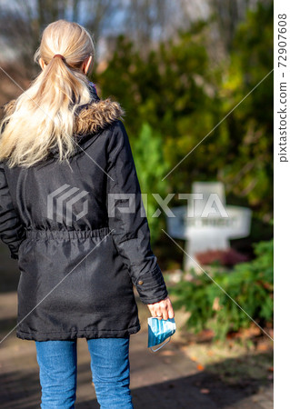 Woman, standing at the grave of family members with a facemask during the pandemic Woman, standing at the grave of family members with a facemask during the pandemic 72907608