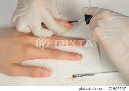 Manicurist master is applying pink gel on client nails in salon, hands closeup. 72907797