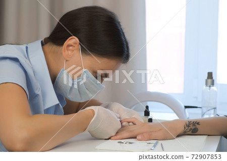 Woman manicurist master cuts cuticle and skin on client's finger using tongs. Woman manicurist master cuts cuticle and skin on client's finger using tongs. 72907853