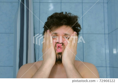Sleepy shaggy young man with headache in bathroom in morning rubs his face. Sleepy shaggy young man with headache in bathroom in morning rubs his face. 72908122