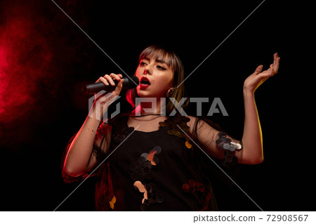 Caucasian female singer portrait isolated on dark studio background in neon light Caucasian female singer portrait isolated on dark studio background in neon light 72908567