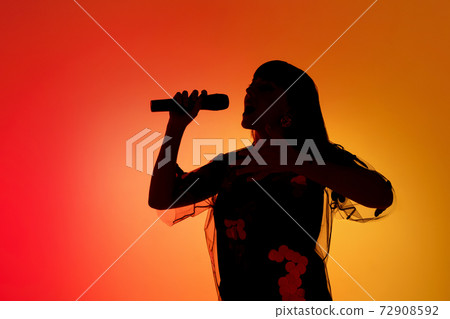 Silhouette of young caucasian female singer isolated on orange gradient studio background in neon light 72908592
