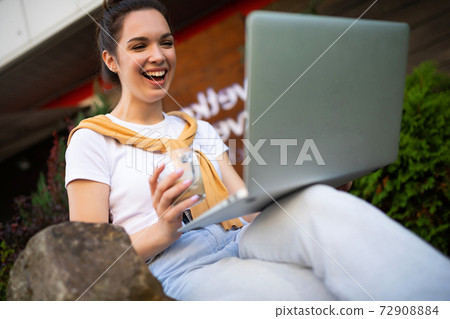 woman student studying on the street sitting with a laptop on her lap woman student studying on the street sitting with a laptop on her lap 72908884