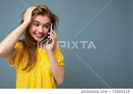 Beautiful positive young blonde woman wearing stylish yellow summer dress standing isolated over 72909116