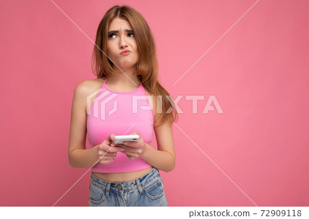 Beautiful thoughtful young blonde woman wearing pink top poising isolated on pink background with 72909118