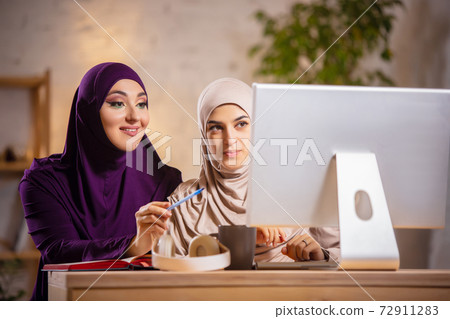 Happy two muslim women at home during lesson, studying near computer, online education Happy two muslim women at home during lesson, studying near computer, online education 72911283