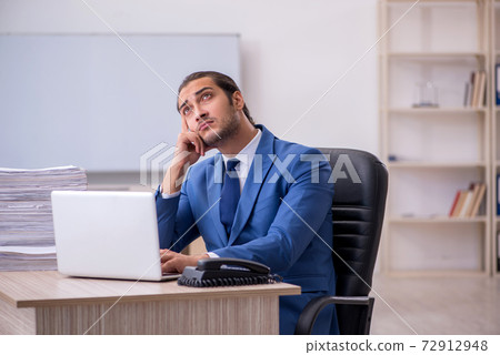 Young male employee and too much work in the office Young male employee and too much work in the office 72912948