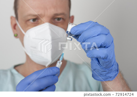 Male nurse with face mask and blue gloves, holding syringe with needle and covid-19 vaccine vial. Medical concept. Male nurse with face mask and blue gloves, holding syringe with needle and covid-19 vaccine vial. Medical concept. 72914724