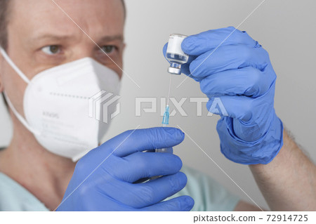 Male nurse with face mask and blue gloves, holding syringe with needle and covid-19 vaccine vial. Medical concept. Male nurse with face mask and blue gloves, holding syringe with needle and covid-19 vaccine vial. Medical concept. 72914725